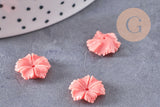 Close-up of EP-Perle fleur résine rose, soft pink flower-shaped resin beads for jewelry making, on a gray stone surface, partially visible white ceramic plate edge.