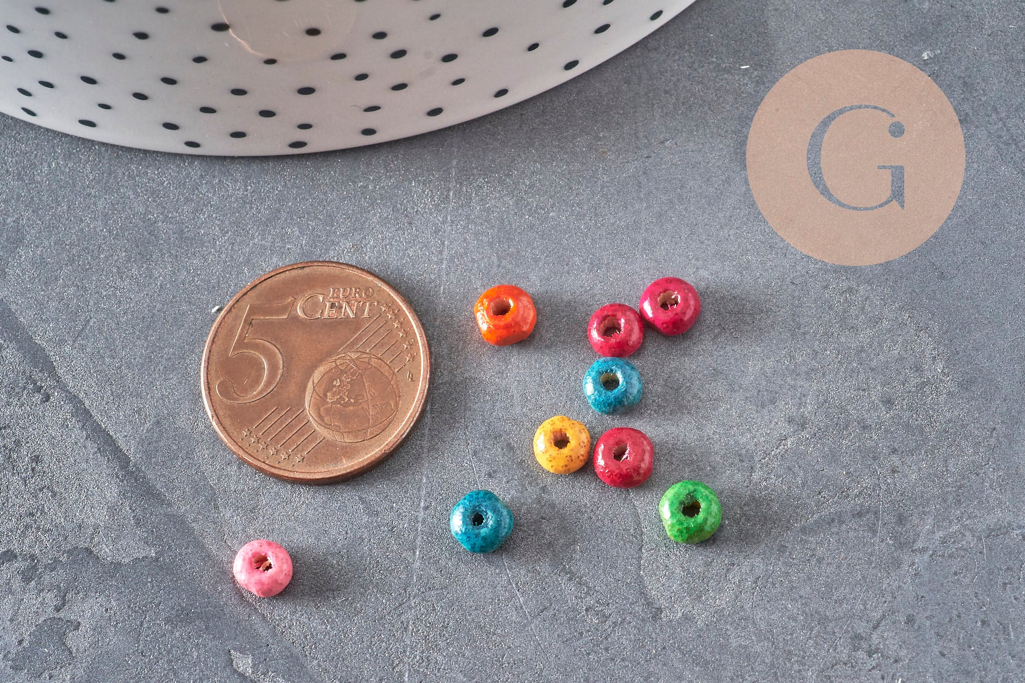 Perles rondelles en bois multicolores de 5x3mm disposées à côté d'une pièce de 5 centimes pour l'échelle.