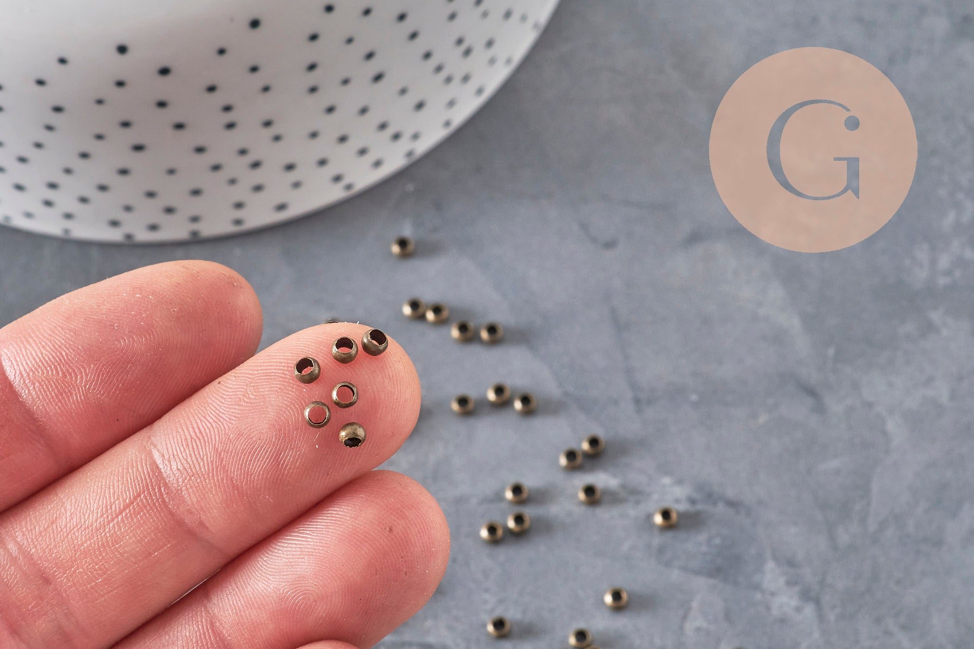 Perles à écraser rondelles en laiton couleur bronze 3x2mm sur des doigts et une surface grise.