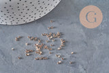 Perles à écraser en laiton or rose 2x1.2mm, dispersées sur une surface grise.